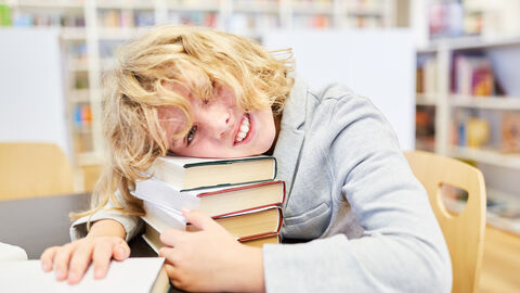 Schüler legt Kopf auf Büchern ab