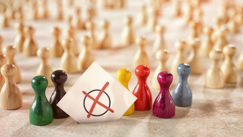 Symbolbild Wahl Symbolbild Wahl: Spielfiguren in verschiedenen Farben versammeln sich um einen Zettel, auf dem ein rotes Kreuz auf einem Kreis zu sehen ist.