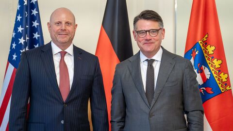 Ministerpräsident Boris Rhein und der neue amerikanische Generalkonsul Brian Heath. Zwei Personen stehen vor Flaggen und schauen in die Kamera.