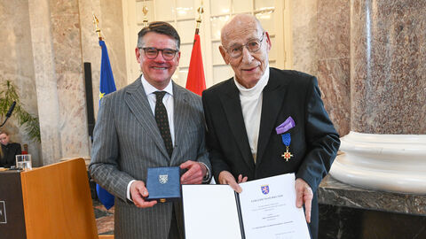 Zwei Männer stehen nebeneinander und halten eine Urkunde hoch.