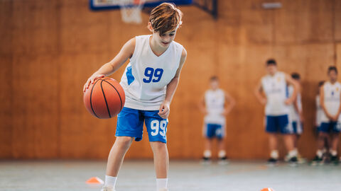 Junge spielt Basketball in der Turnhalle