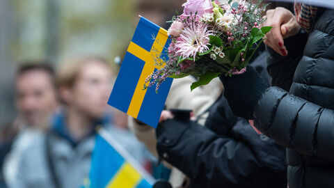 Schwedische Flagge beim Empfang der Kronprinzessin Victoria von Schweden. Nahaufnahme einer schwedischen Flagge in der Hand einer Person. Dazu hält diese Person auch noch einen Blumenstrauß in der Hand.