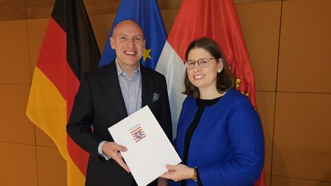 Ein Mann und eine Frau stehen nebeneinander und halten gemeinsam eine Urkunde hoch.