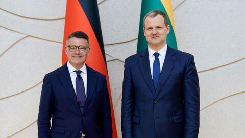 Zwei Männer stehen vor der deutschen und litauischen Landesflagge nebeneinander.