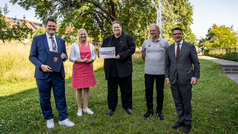(v.r.n.l.): Ministerpräsident Boris Rhein mit Jugendleiter Dirk Münkel und Sebastian Heil, erster Vorsitzender des Sportclubs 1959 Dortelweil e.V., Sportministerin Diana Stolz und Bad Vilbels Bürgermeister Sebastian Wysocki bei der Bescheidübergabe auf dem Hessentag in Bad Vilbel.  Fünf Menschen stehen nebeneinander auf einer Wiese. Die mittlere Person hält einen Zuwendungsbescheid in der Hand.